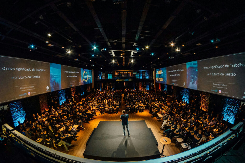 gestão condominial - palestrante em auditório corporativo durante evento Master Síndico Experience com plateia atenta e telões iluminados